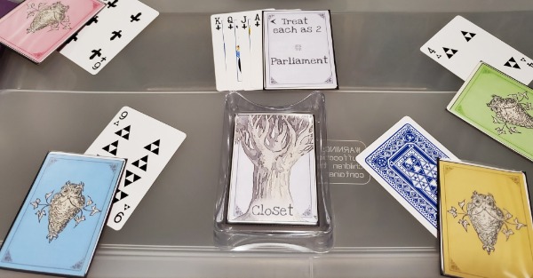 4 Owl cards over some numbered poker cards, one of which face down, and 4 sword suited cards under a parliament card positioned above an empty closet.