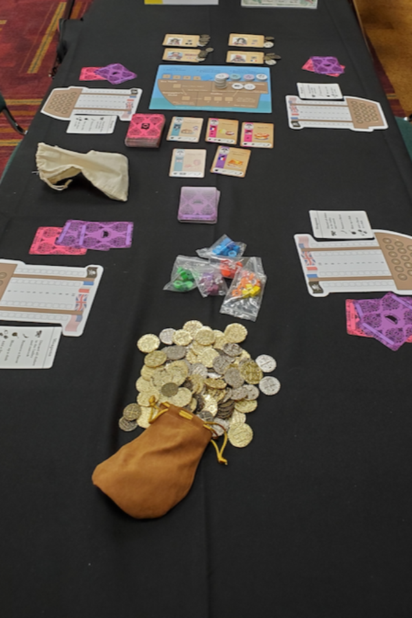 A table with a black table cloth, central board with a ship on it, 4 player mats shaped like ships, and 5 cards laid out.