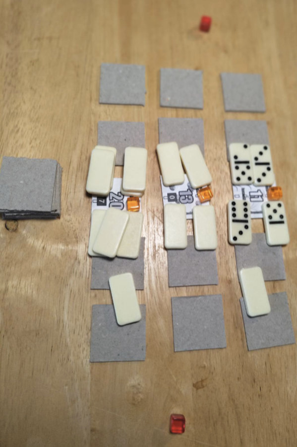 Print and play prototype in action! A grid of tiles, some face down with dominoes and cubes on them.