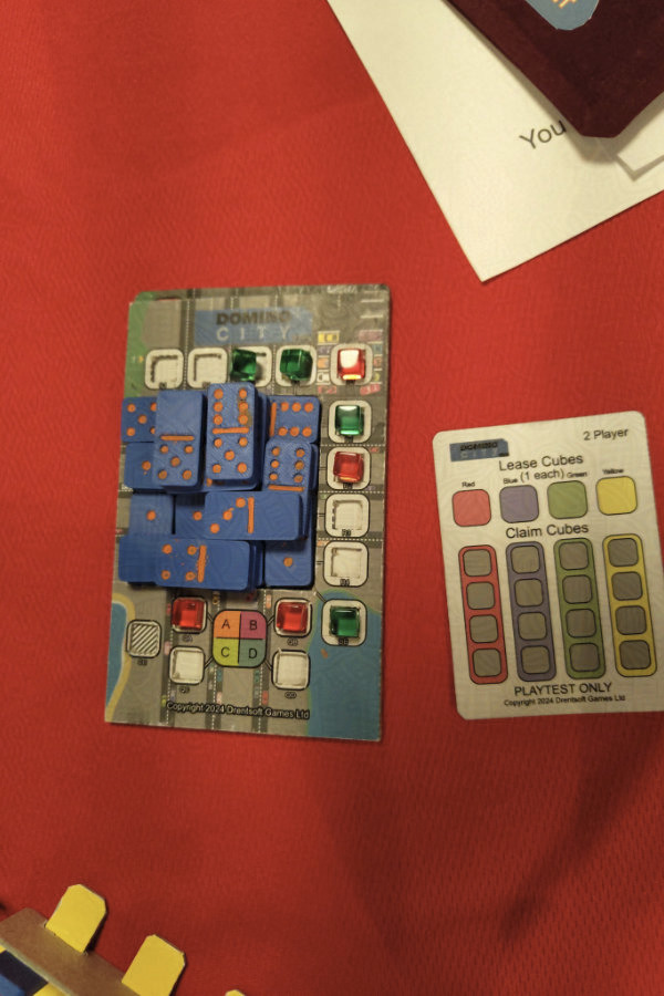 The game being played at Dragonmeet Playtest UK. Dominoes are stacked in the middle of the board. Game is finished. Red scored 52, green score 58. Game was played without lease cubes.